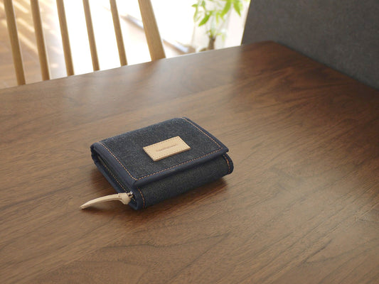 濃い色の木のテーブルに置いた、濃紺のデニムのコンパクトな折り財布