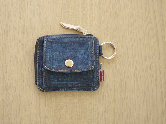 明るい木の机に置いた、藍色のデニムの小さな財布を真上から。金具のリングと革の引き手が付いている